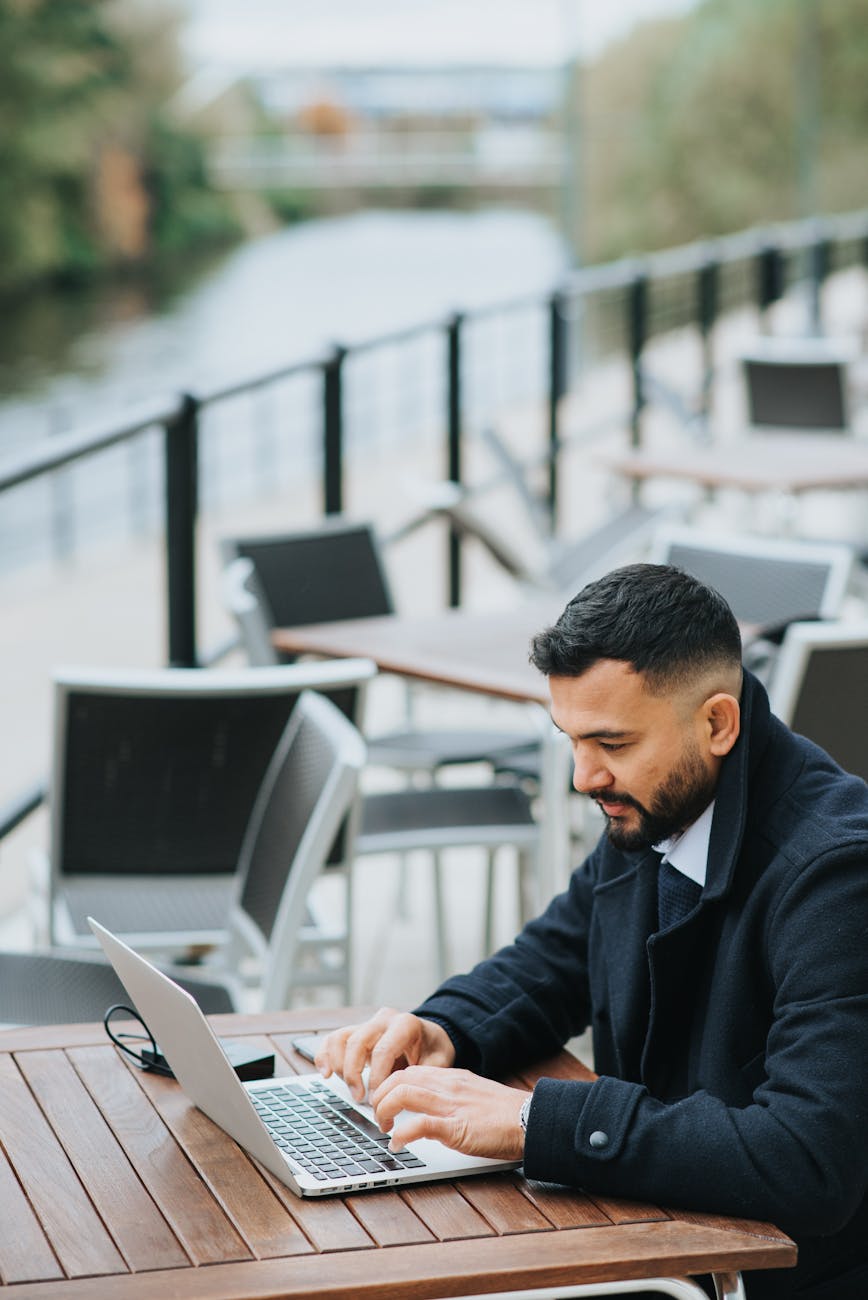serious ethnic businessman typing on laptop on cafe terrace